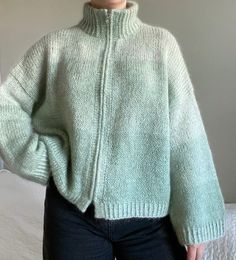 a woman standing in front of a bed wearing a green sweater