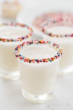 three glasses filled with milk and sprinkles on top of a white counter