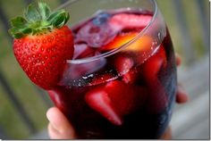 a close up of a person holding a drink with strawberries on the rim and ice