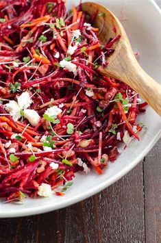 shredded carrots and beets in a white bowl with a wooden spoon on the side