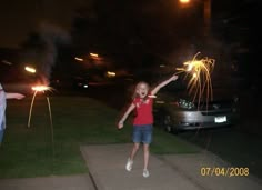 two people standing on a sidewalk with sparklers in the air and one person pointing at something