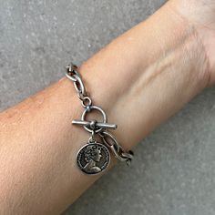 A beautiful silver coin bracelet. This silver bracelet with coin pendant is easy to match and will upgrade any outfit. This silver toggle clasp bracelet has unique eye shaped links. Please note: length doesn't include the heart pendant. For reference: in photos I'm wearing a 8" long bracelet. This bracelet is available in available in gold as well. Materials: Silver plated brass and elements - oxidized finish Gold plated brass and elements - shiny finish Measurements: Chain width: 0.3"/8mm Clasp Silver Bracelets With Coin Pendant For Gift, Silver Bracelets With Coin Pendant As Gift, Symbolic Coin-shaped Sterling Silver Jewelry, Vintage Bracelet With Toggle Clasp, Vintage Silver Coin Bracelet, Antique Coin-shaped Metal Jewelry, Antique Coin-shaped Sterling Silver Jewelry, Toggle Clasp Bracelet, Roman Coins