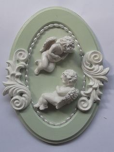 two cherubs are sitting in the center of an oval frame with swirl designs