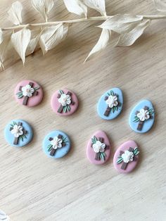 six buttons with flowers on them sitting on top of a wooden table next to leaves