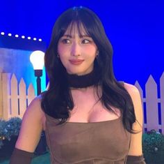 a woman with long black hair wearing a brown dress and posing for the camera in front of a blue background