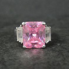 This beautiful estate ring is sterling silver with a 10x12mm pink cubic zirconia accented by clear cubic zirconias. The face of this ring measures 1/2 of an inch north to south with a rise of 9mm off the finger. Size: 8 Marks: 925 Condition: Excellent Pink Sterling Silver Crystal Ring With Center Stone, Pink Sterling Silver Diamond Ring With Accent Stones, Pink Sterling Silver Crystal Ring For Formal Occasions, Pink Emerald Cut Sterling Silver Ring, Classic Pink Diamond Ring Vs Clarity, Classic Pink Diamond Ring With Vs Clarity, Pink Cubic Zirconia Crystal Ring, Fine Jewelry, Pink Emerald Cut Cubic Zirconia Jewelry, Fine Jewelry Pink Ring Stamped 925