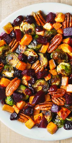 a white plate topped with roasted vegetables and pecans on top of a wooden table