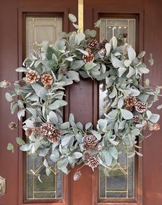 a wreath with pine cones and eucalyptus leaves is hanging on the front door to welcome guests