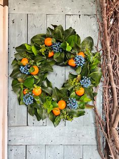 a wreath with oranges, blue berries and green leaves hangs on a wooden wall