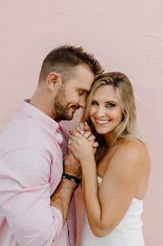 a man and woman standing next to each other in front of a pink wall holding hands