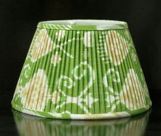 a green and white lamp shade sitting on top of a reflective surface with the reflection of it's lampshade