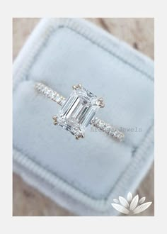 an emerald cut diamond engagement ring on top of a white velvet box with diamonds around it