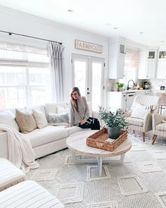 a woman sitting on a couch in a living room with white furniture and rugs