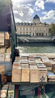 many books are stacked on top of each other in front of a river and building