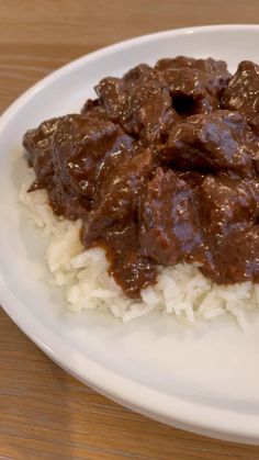 a white plate topped with rice covered in beef and gravy on top of a wooden table