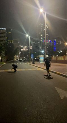 two skateboarders are riding down the street at night