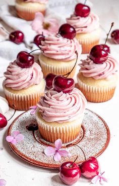 cupcakes with pink frosting and cherries on a plate