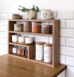 a wooden shelf filled with jars and spices on top of a counter next to a white brick wall