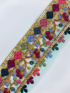 an embroidered ribbon with gold chains and colorful flowers on white background, close up view