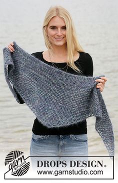 a woman holding up a shawl in front of the water with her hands on her hips