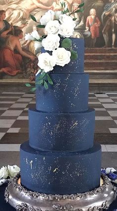 a blue wedding cake with white flowers on the top and bottom, sitting on a checkered tablecloth