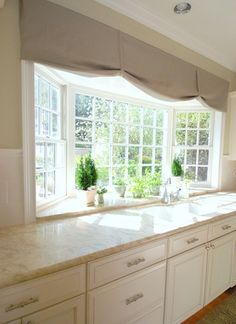 an empty kitchen with white cabinets and marble counter tops in front of two large windows