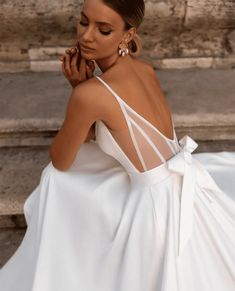 a woman in a white dress posing for the camera with her hand on her cheek