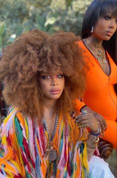 two women with afro hair sitting next to each other and one is wearing an orange shirt