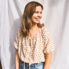 a woman standing in front of a white backdrop wearing jeans and a polka dot blouse