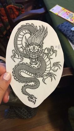 a person holding up a white sticker with a dragon on it's side