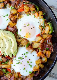 two fried eggs on top of potatoes in a skillet with avocado and sour cream