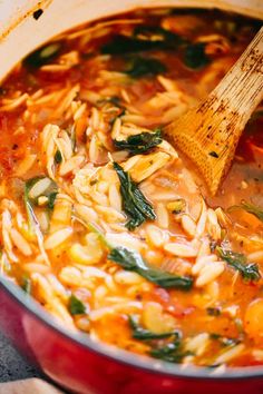 a red pot filled with pasta and spinach being stirred by a wooden ladle