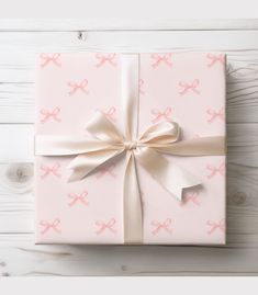 a pink gift box with white ribbon and bows on it sitting on top of a wooden table