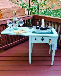 a blue table with two wine glasses and bottles on it sitting on a wooden deck