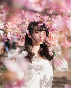 a woman in white shirt standing under pink flowers