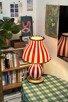 a red and white lamp sitting on top of a table next to a book shelf