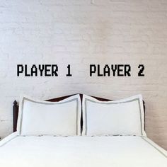 a bed with white sheets and pillows next to a brick wall that says player 1, player 2