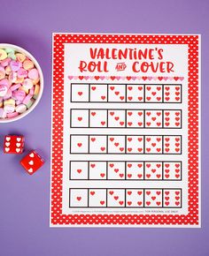 a valentine's roll and cover game next to two dices on a purple surface