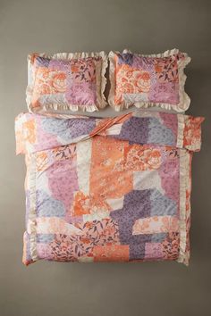 an orange and pink quilted bed with ruffles on the pillowcase, along with two matching pillows