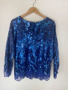 The captivating Blue Sequin Blouse -- designed to mesmerize and elevate your look to new heights. This stunning blouse, in good vintage condition, boasts a few small discolorations on the sequins located on the upper rear neckline. However, rest assured that these minor imperfections do not detract from the overall beauty of this eye-catching piece. Crafted in size L, this blouse is intentionally oversized, delivering a relaxed and comfortable fit for everyone. The sheer fabric and intricate hand-beaded detailing on the lower shirt body and sleeves exude an air of elegance and sophistication. The impeccable condition of the beads and sequins ensures that they catch the light, creating a mesmerizing sparkle wherever you go. Prepare to turn heads and make a stylish statement with the Blue Se Festive Blue Sequined Blouse, Blue Embellished Party Blouse, Festive Blue Sequin Blouse, Festive Blue Blouse With Sequins, Blue Embellished Top For Evening, Glamorous Blue Sequined Tops, Glamorous Blue Tops For Party Season, Party Blouse With Sequins, Blue Embellished Long Sleeve Top