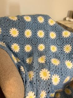 a crocheted blanket with yellow and white flowers on it sitting on a chair