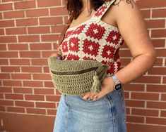 a woman wearing a red and white crochet top is holding a green purse