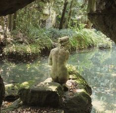 a statue sitting on top of a rock in the middle of a river surrounded by trees