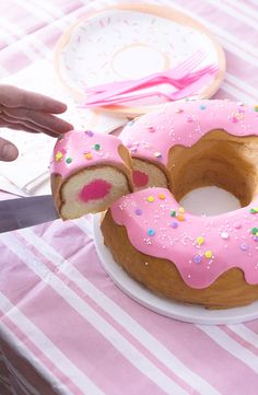 a pink frosted donut on a plate with a slice taken out of it