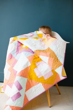 a baby is sleeping under a quilt on a chair