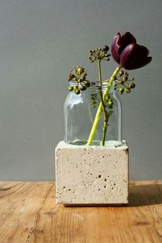 two flowers are in a glass vase on a wooden table with concrete blocks and water