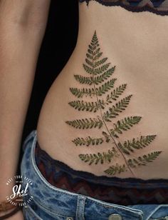 a close up of a person's stomach with a fern tattoo on her side