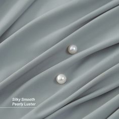 two white pearls are sitting on top of a gray fabric with the words silky smooth pearly luster