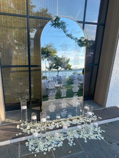 a large mirror sitting on the side of a building next to candles and flowers in front of it