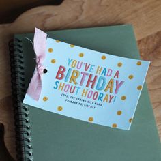 a birthday card on top of a spiral notebook with a pink ribbon attached to it